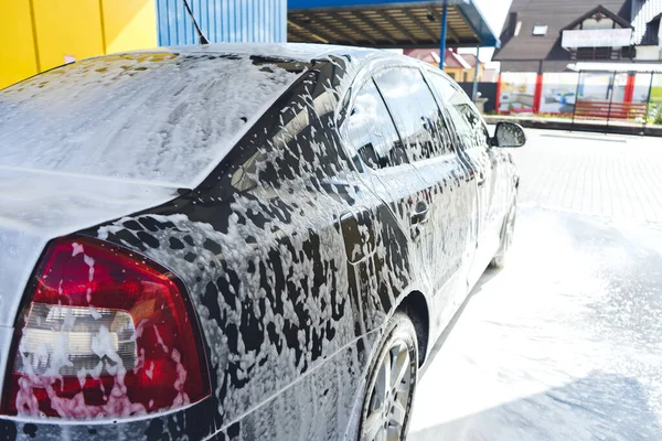 Black car in white foam on a manual car wash. Gray car washed in white foam. Car at the car wash