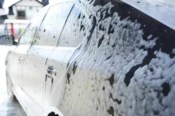 Black car in white foam on a manual car wash. Gray car washed in white foam. Auto at the car wash.