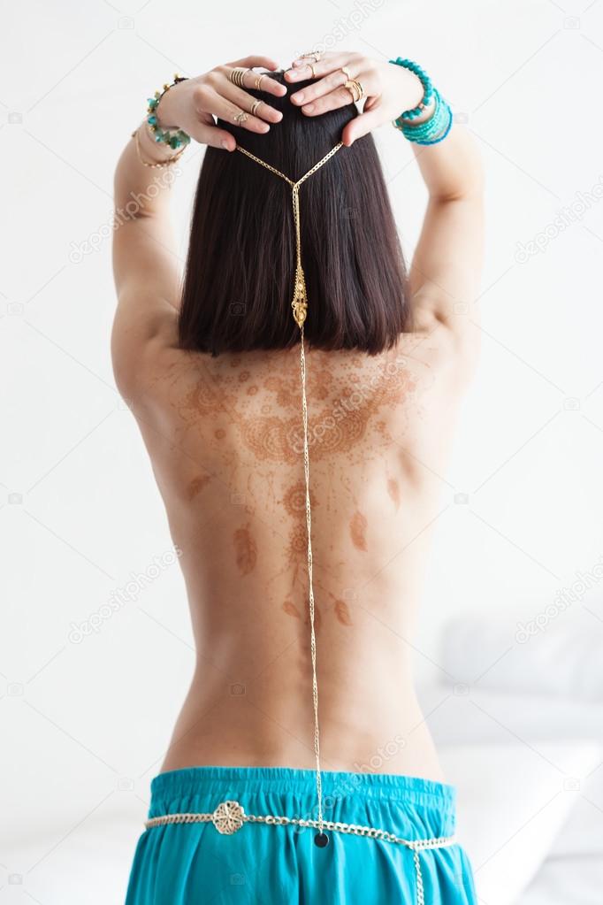 Attractive an slim woman in oriental garment and golden jewelry with henna drawnings on her back.