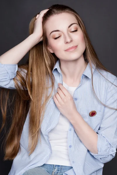 Portrait of a beautiful young blonde girl. She is wearing a denim shirt and a white T-shirt.