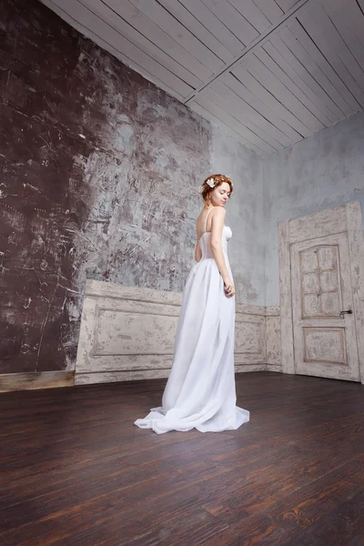 Bella giovane sposa in un abito da sposa lungo è in piedi in una stanza vuota — Foto Stock