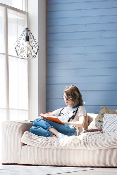 Young smart female student studying diligently at home near large window. Balcony, sofa, soft pillows.