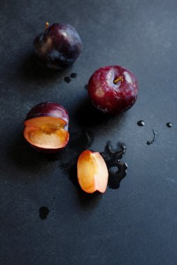 Siyah bir masanın üzerinde yatan üç olgun sulu homegrown Erik. Yaz Köyü
