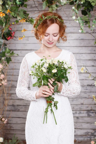 Giovane sposa dai capelli rossi in una ghirlanda verde con un mazzo di fiori bianchi — Foto Stock