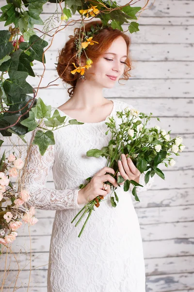 Giovane sposa dai capelli rossi in un semplice abito di pizzo sta tenendo un bouquet — Foto Stock