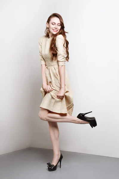 Attraente giovane donna in abito d'oro sorride e si erge in posa di moda — Foto Stock