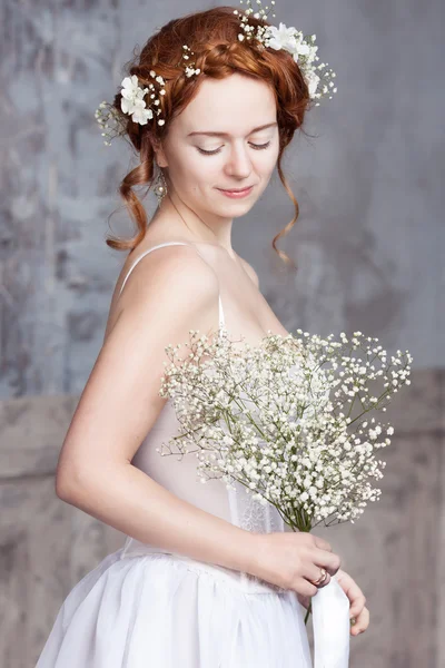 Giovane sposa dai capelli rossi in elegante abito da sposa bianco. Sta in piedi, i suoi occhi sono chiusi da sogno, tiene in mano un mazzo di fiori bianchi . — Foto Stock