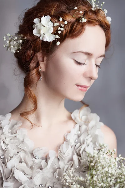 Portrait of beautiful red-haired bride. She has a perfect pale skin with delicate blush. White flowers in her hair.