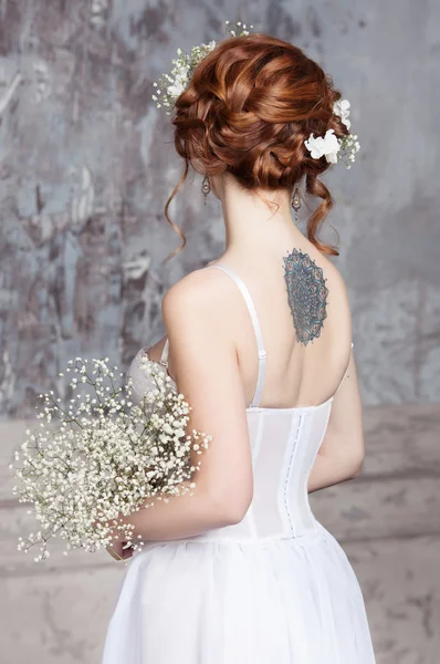 Young red-haired bride in elegant wedding dress. She stands with her back to the viewer.