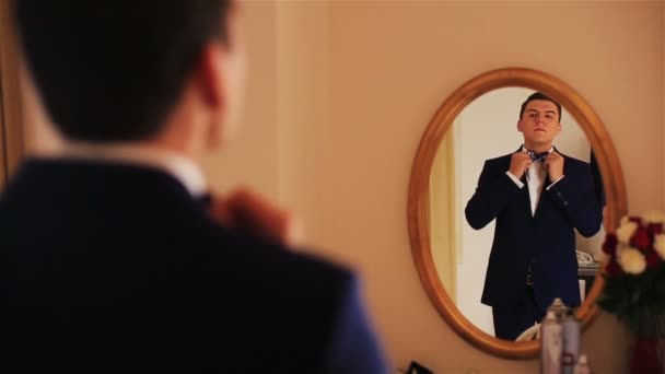 Knappe bruidegom op reflectie in de spiegel kijkt en corrigeert de bowtie — Stockvideo