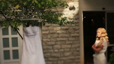 Sarı gelin gülümseyen gözlerle beyaz elbise içinde büyüleyici bir ağaç arka plan üzerinde asılı gelinlik kapalı