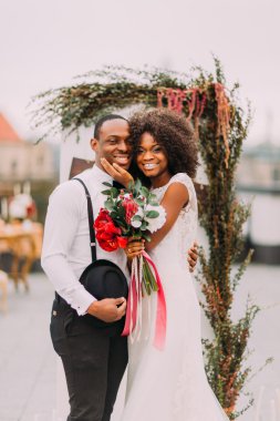 Mutlu siyah yeni evliler gülümseyen ve onların düğün töreni sırasında çatıda sarılma