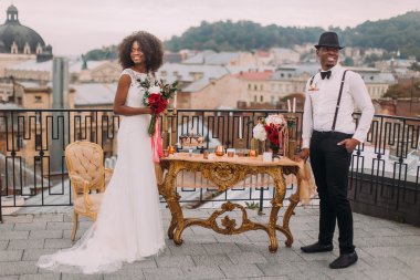 Happy black newlyweds happily smiling on the terrace near the wedding table