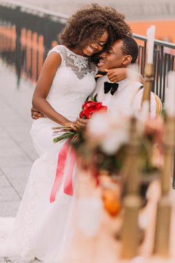 Black cheerful wedding couple softly hugging on the terrace with amazing view on Lviv ancient architecture. Wedding day