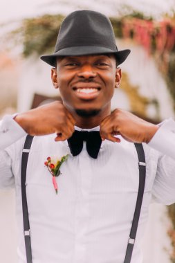 Happy african groom sincerely smiling and corrects his bowtie clipart
