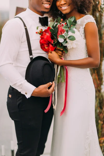 Young pretty black bride and groom happily smiling and holding a bouquet in half length