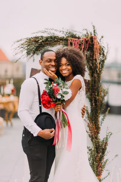 Mutlu siyah yeni evliler gülümseyen ve onların düğün töreni sırasında çatıda sarılma