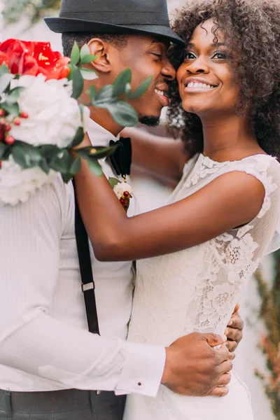 Beautiful african bride and happy groonm in black hat  embracing on the weddig ceremont close up