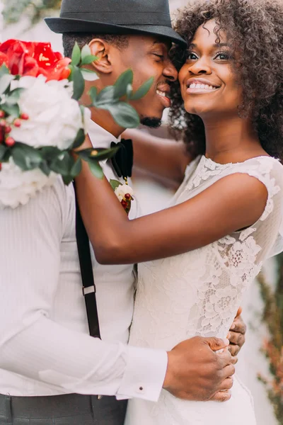 Beautiful african bride and happy groonm in black hat  embracing on the weddig ceremont close up — Stok fotoğraf