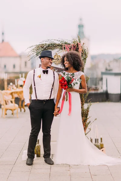 Encantadores recién casados africanos se miran soñadoramente. Día de la boda. En la azotea. Arquitectura de Lviv en el fondo — Foto de Stock