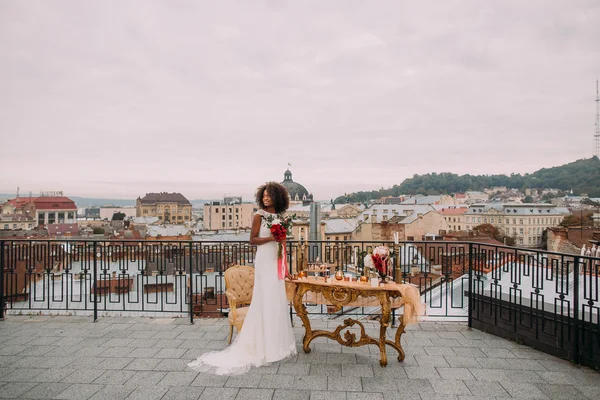 Hübsche afrikanische Braut mit Brautstrauß in den Händen auf der Terrasse stehend — Stockfoto