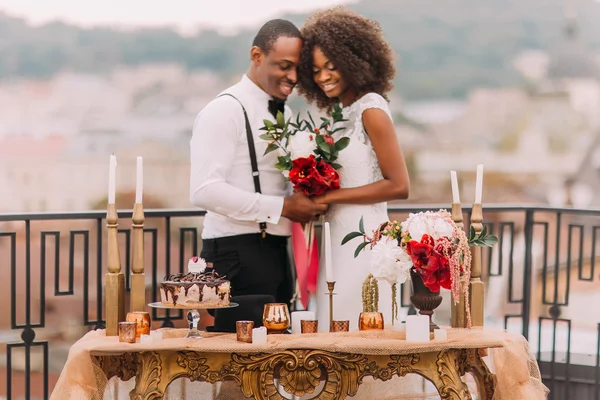 Romantici sposi africani sulla terrazza. Lussuoso tavolo dorato in stile orientale in primo piano — Foto Stock