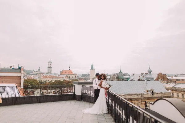 Africká svatební dvojice na střeše. Úžasná Evropská Lvova architektura na pozadí — Stock fotografie