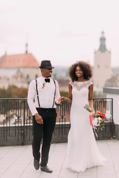 Mooie Afrikaanse bruiloft paar houden handen op het dak met uitzicht op Lviv stad architectuur — Stockfoto