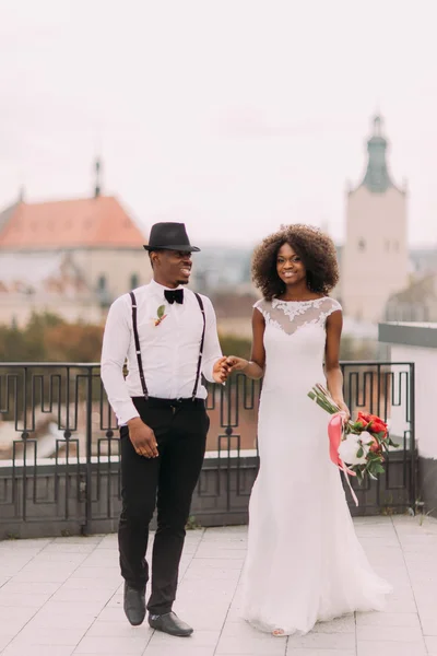 Casal de casamento africano encantador de mãos dadas no telhado com vista sobre a arquitetura da cidade de Lviv — Fotografia de Stock