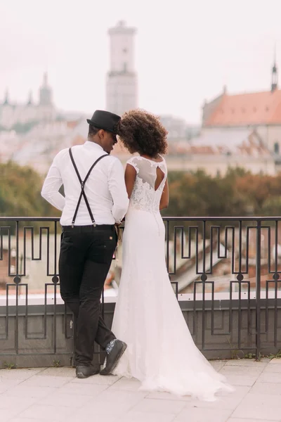 Beatiful african newlyweds holding each other on the terrace with amazing Lviv architecture on background