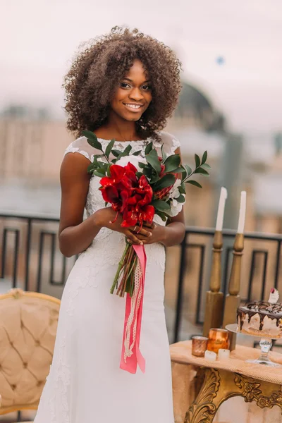 Afrikalı gelin neşeyle elinde kırmızı çiçek buketi ile gülümseyen