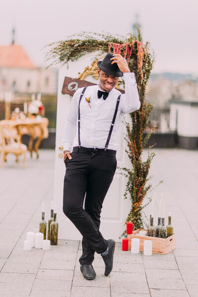 Handsome african groom in suspenders takes off his hat