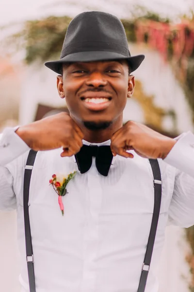 Happy african groom sincerely smiling and corrects his bowtie — Stock Photo, Image