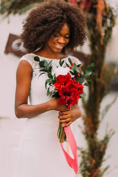 Schöne afrikanische Braut glücklich lächelnd mit einem Strauß roter Blumen in den Händen — Stockfoto