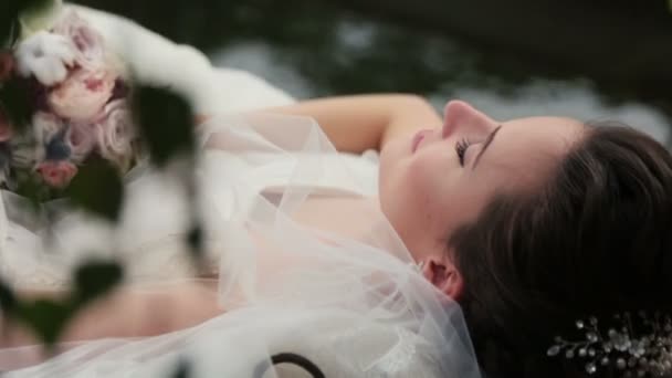 Чарівна брюнетка наречена лежить у човні з закритими очима крупним планом. Весільний букет в руках — стокове відео