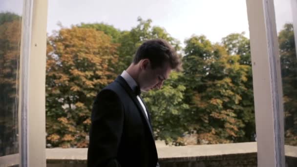 Handsome groom dreamily  looks through a window — Stock Video
