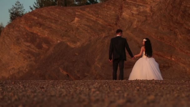 Bella coppia di sposi che cammina e si tiene per mano nelle montagne rosse — Video Stock