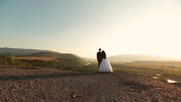 Hermosa pareja de boda se abraza en las montañas en la vista posterior. Luna de miel — Vídeos de Stock