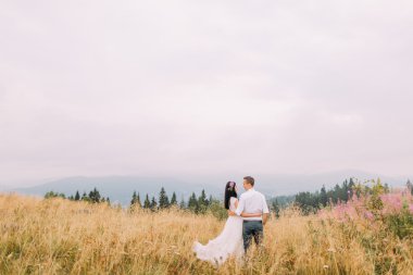 Güzel düğün çifti sahada sarıl. Dağlar arka plan
