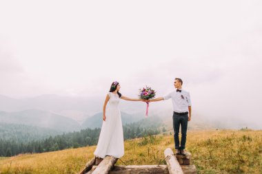 Buket ahşap köprü üzerinde tutarak Düğün çifti. Dağlarda balayı