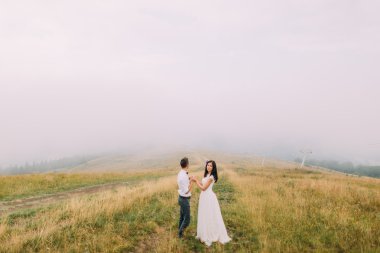 Elele ve geçişte ayakta Düğün çifti. Puslu dağlar arka plan