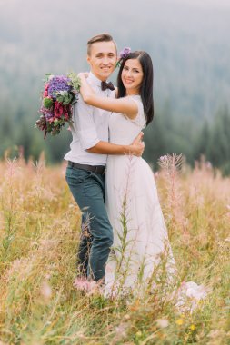 Mutlu gelin ve damat kamera için poz. Arka planda dağlar