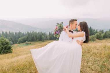 Yakışıklı damat büyüleyici gelini elinde tutar. Dağlar balayı