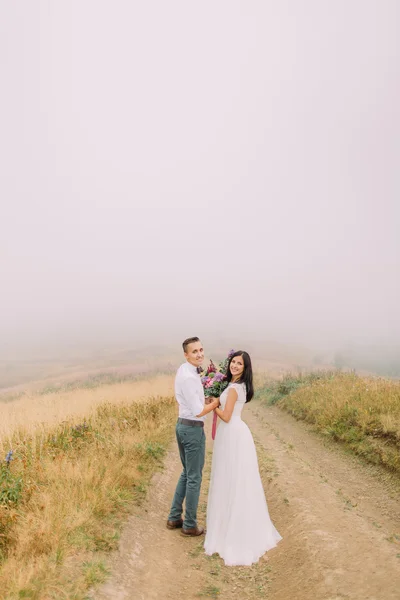 Casamento casal posando no caminho. Misty montanhas fundo — Fotografia de Stock
