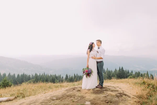 Bonito noivo abraça noiva no pico da montanha — Fotografia de Stock