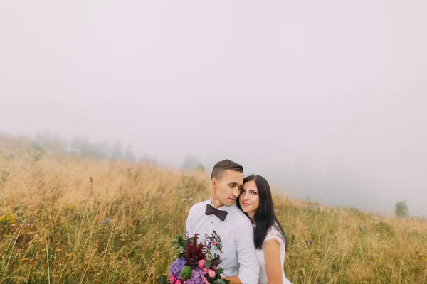 Pareja de bodas abrazos suavemente. Montañas brumosas en el fondo — Foto de Stock