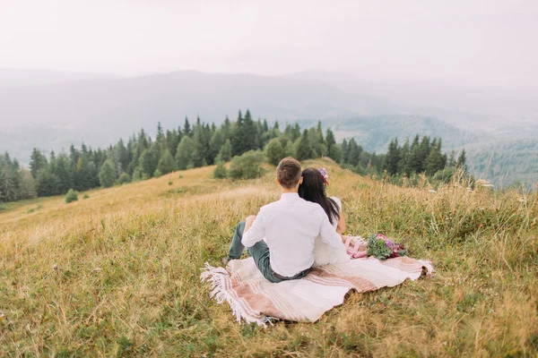 Pareja sentada en cuadros en la cima de la montaña — Foto de Stock