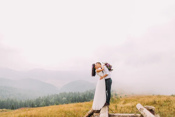 美しい結婚式のカップルは、木製の橋にキスします。山で霧の日 — ストック写真