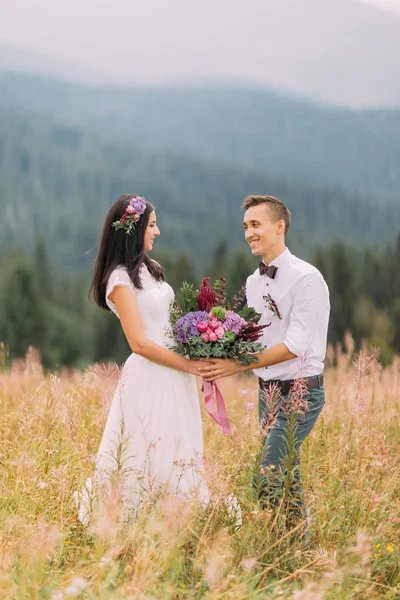 Schönes Hochzeitspaar mit einem Strauß lila Blumen in den alpinen Bergen. Flitterwochen — Stockfoto