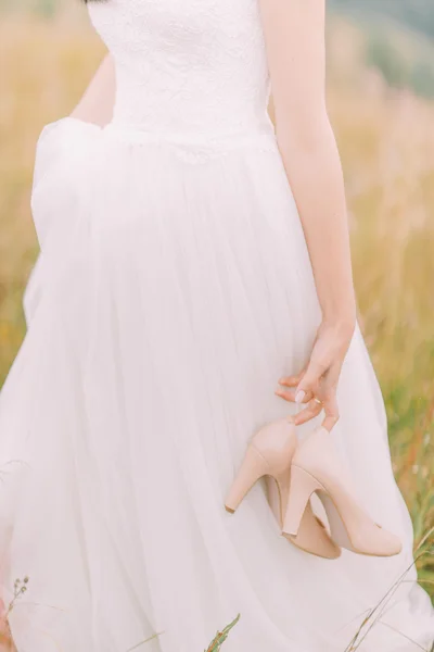 Hermosa novia camina con tacones en las manos. Campo verde de cerca — Foto de Stock